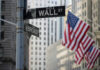 Street signs for Wall Street and Broad Street with American flags in the background