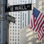 Street signs for Wall Street and Broad Street with American flags in the background