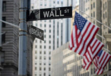 Street signs for Wall Street and Broad Street with American flags in the background