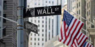 Street signs for Wall Street and Broad Street with American flags in the background
