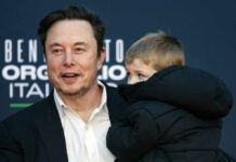 A man in a black suit holding a child in a coat at a public event