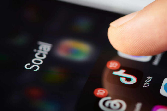 Close-up of a finger tapping a TikTok icon on a smartphone screen with social media labels
