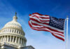 American flag waving in front of the U.S. Capitol building under a clear blue sky