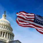 American flag waving in front of the U.S. Capitol building under a clear blue sky