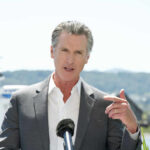 A man in a suit speaking at a podium with a microphone outdoors