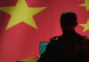 Silhouette of a military personnel working on a laptop in front of a Chinese flag