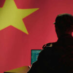 Silhouette of a military personnel working on a laptop in front of a Chinese flag