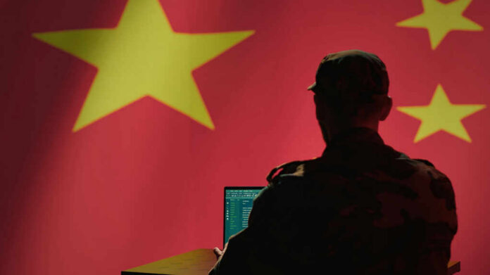 Silhouette of a military personnel working on a laptop in front of a Chinese flag