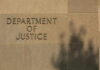 Sign reading Department of Justice on a stone wall with a shadow
