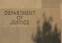 Sign reading Department of Justice on a stone wall with a shadow
