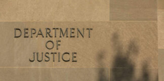 Sign reading Department of Justice on a stone wall with a shadow