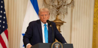 A political figure speaking at a podium with American and Israeli flags in the background