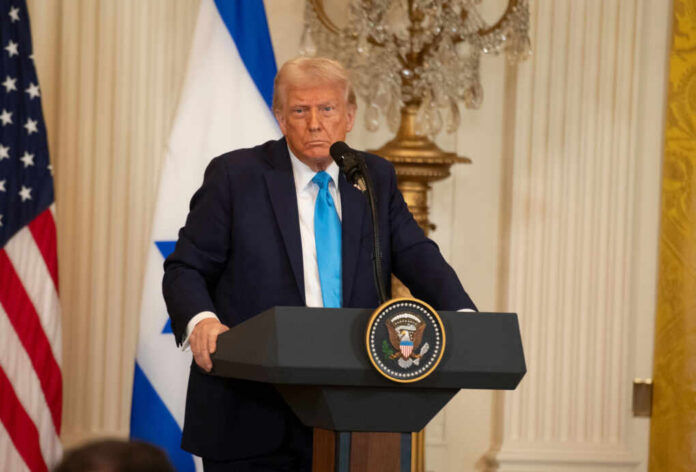 A political figure speaking at a podium with American and Israeli flags in the background