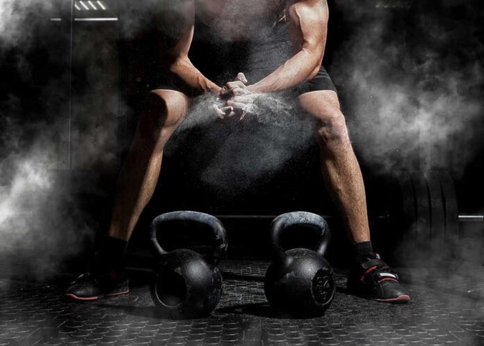 Athlete preparing to lift kettlebells in a gym with chalk dust in the air