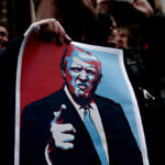 A person holding a protest sign featuring a stylized illustration of a man with a serious expression
