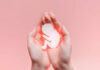 Hands holding a paper cutout of a fetus against a pink background