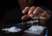 A hand reaching for a syringe next to a pile of white powder