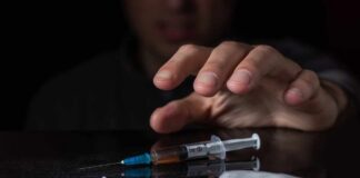 A hand reaching for a syringe next to a pile of white powder