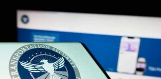Close-up of a mobile device displaying the TSA logo with a blurred background of a website
