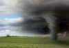 A tornado forming under dark storm clouds in an open field