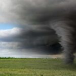 A tornado forming under dark storm clouds in an open field