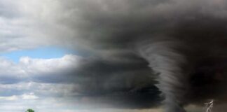 A tornado forming under dark storm clouds in an open field