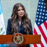 A woman speaking at a podium with flags in the background