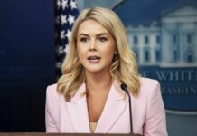 A woman in a pink blazer speaking at a podium during a press briefing