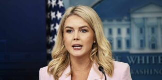 A woman in a pink blazer speaking at a podium during a press briefing