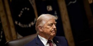 A political figure seated with a serious expression in a formal setting