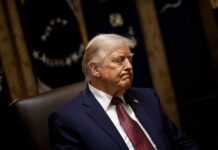 A political figure seated with a serious expression in a formal setting