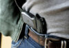 A handgun partially visible in a belt holster worn by a person in casual clothing