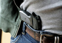 A handgun partially visible in a belt holster worn by a person in casual clothing