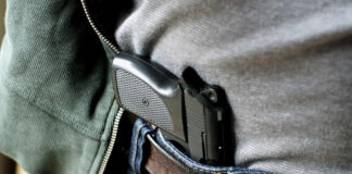 A handgun partially visible in a belt holster worn by a person in casual clothing