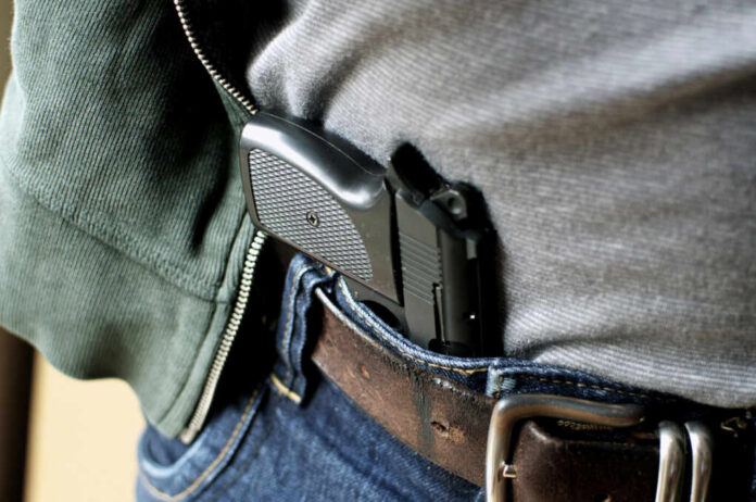 A handgun partially visible in a belt holster worn by a person in casual clothing
