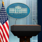 Podium with microphones in front of the White House seal and an American flag