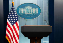 Podium with microphones in front of the White House seal and an American flag