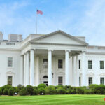 The White House with an American flag flying above, surrounded by greenery