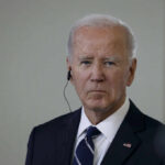 A serious-looking man in a suit with an earpiece, standing indoors