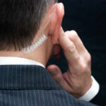 Close-up of a man in a suit with an earpiece, indicating a security role