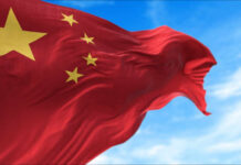 Waving Chinese flag with five yellow stars against a blue sky