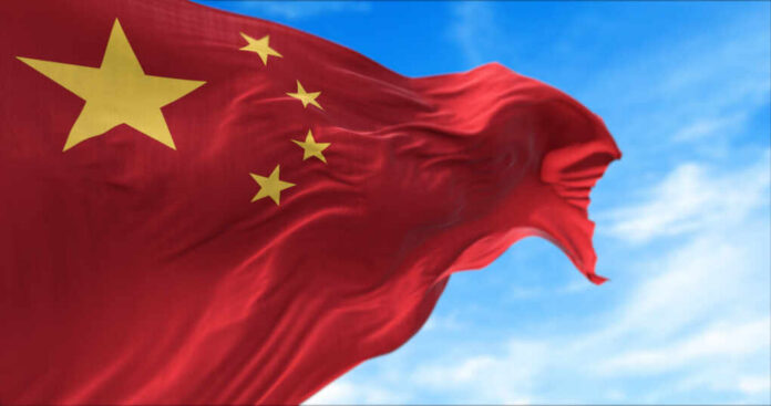 Waving Chinese flag with five yellow stars against a blue sky