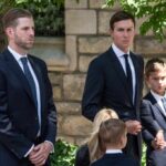 A group of men and children in formal attire standing outdoors, appearing serious