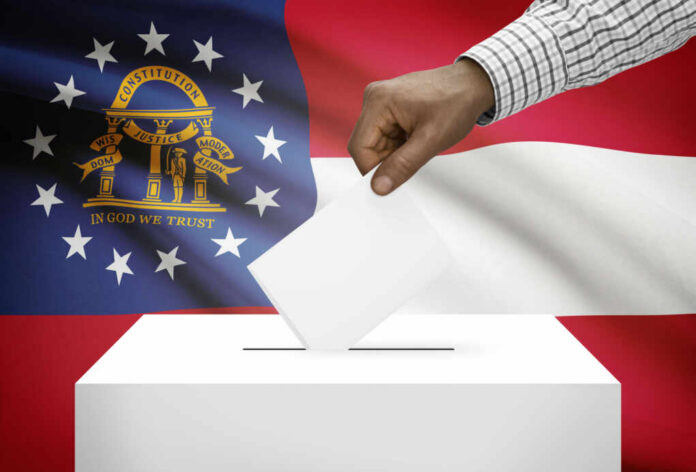 shutterstock_244412023.jpg A hand placing a ballot into a ballot box with the Georgia state flag in the background