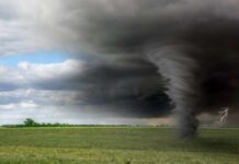 A tornado forming under dark storm clouds in an open field