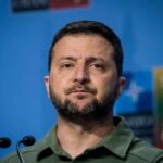 A political leader speaking at a press conference with a serious expression