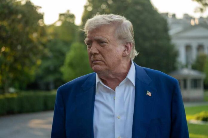 A political figure with a serious expression standing outdoors near the White House