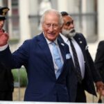 King Charles’ Sharp Jab Steals Dinner A smiling man in a blue suit waving at the camera