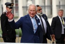 A smiling man in a blue suit waving at the camera