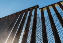 View of a border wall with a chain-link fence against a clear blue sky